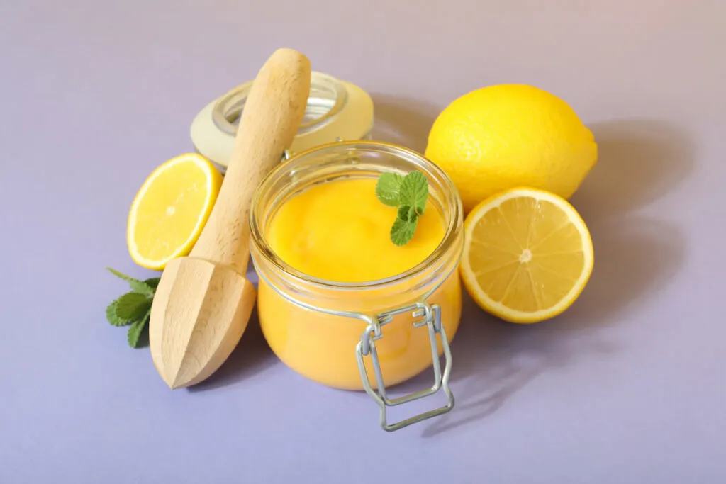 Lemon curd in a small glass jar and fresh lemons around it