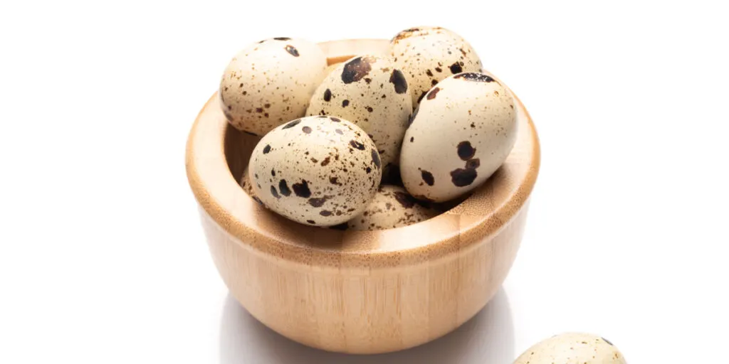 Quail eggs in the wooden bowl isolated on white background