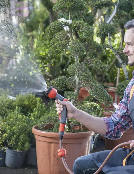 man holding a hose watering all plants