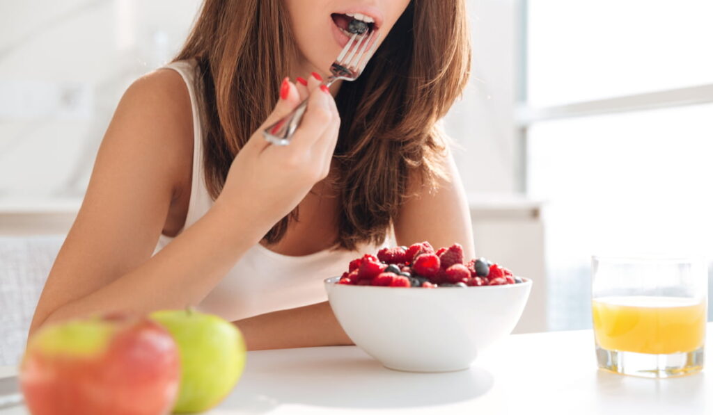 woman eating a bowl full of berries with a glass of orange juice