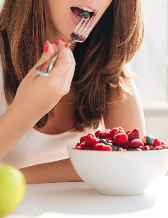 woman eating a bowl full of berries with a glass of orange juice