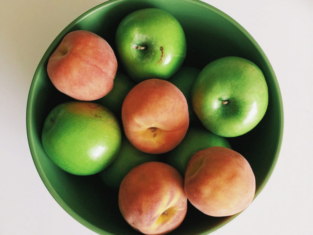 A green bowl filled with peaches and apples 
