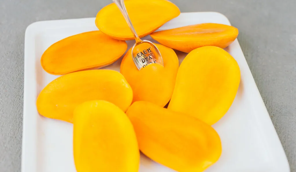 sliced ripe mangoes on a white tray with a spoon stuck on it 