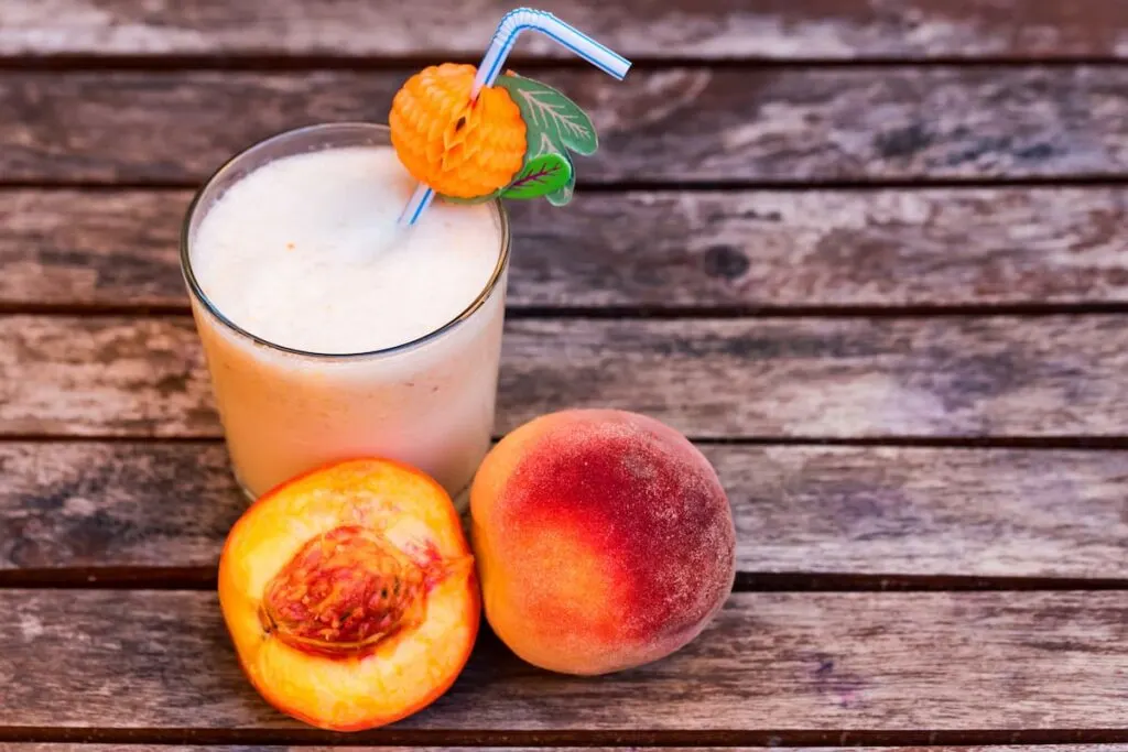 glass of peach yoghurt and peaches on wooden table 