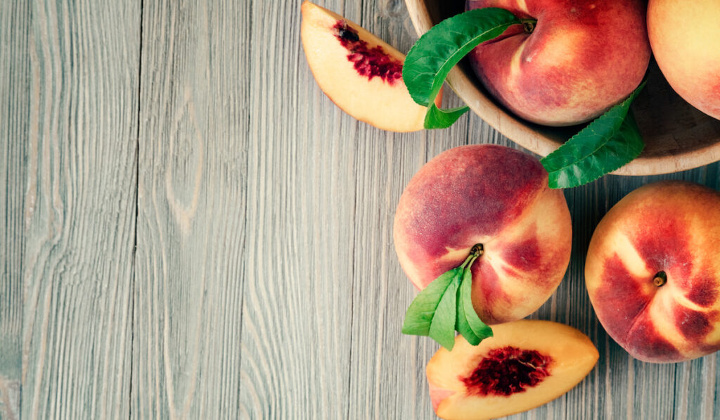 whole and sliced peaches with leaves on wooden background