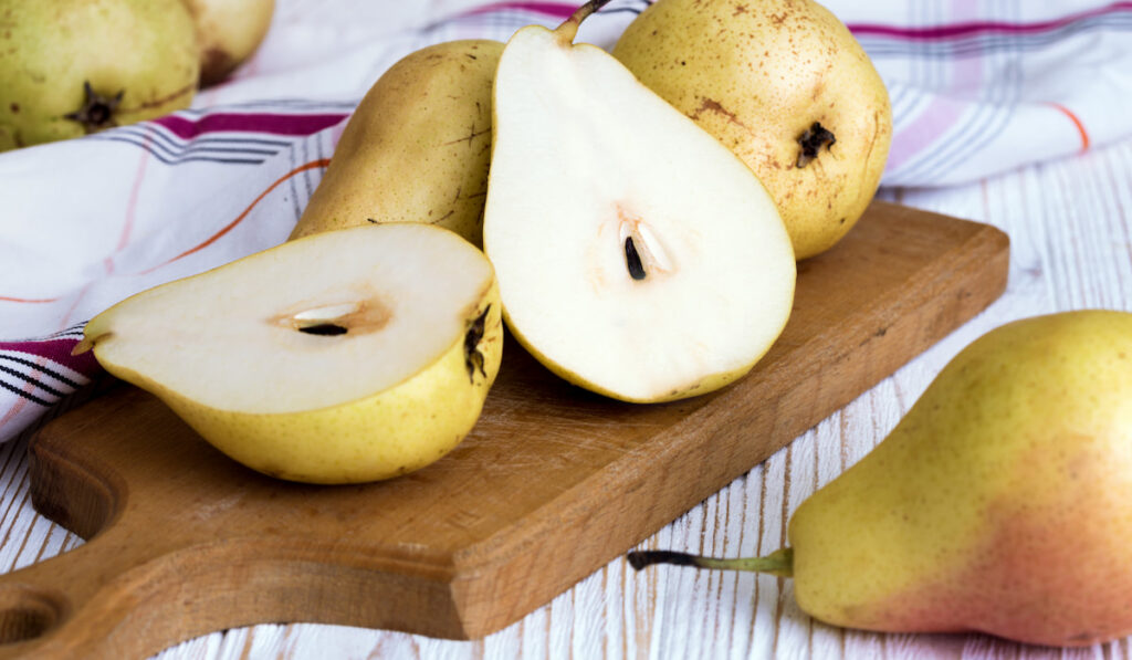 whole and sliced pears on a wooden chopping board