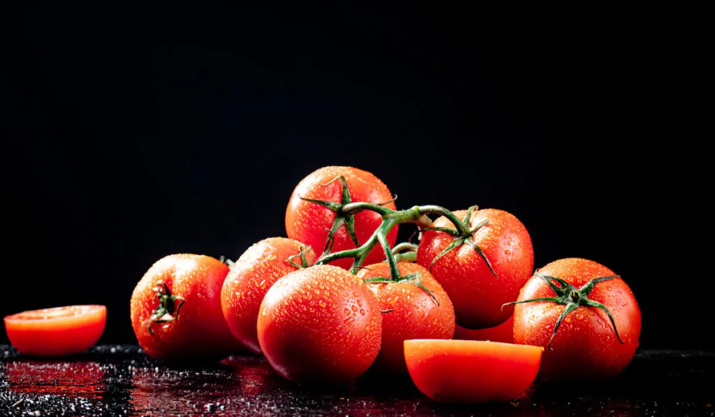 whole and sliced tomatoes on black background