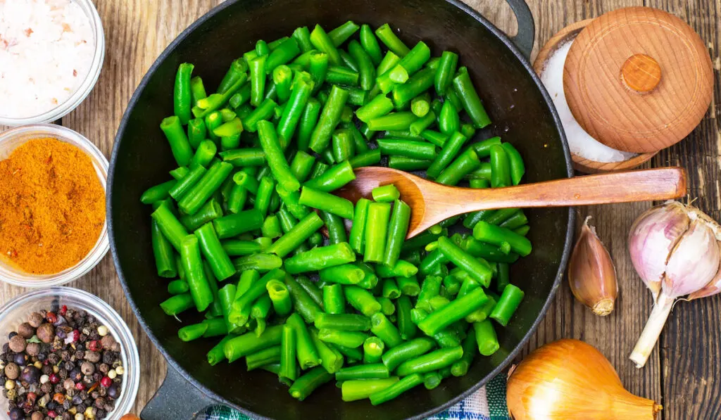 Green Beans on cast-iron frying pan with cooking aromatics on the table