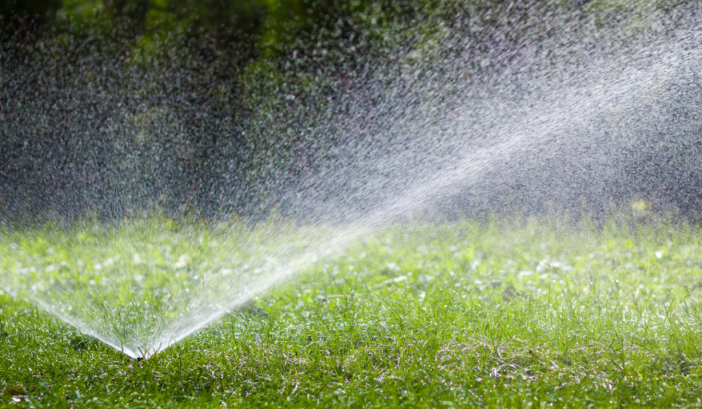 Lawn water sprinkler spraying water over grass in garden on a hot summer day.