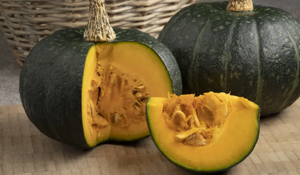 Whole and sliced Kabocha Squash on wooden ground with wooden basket on the background