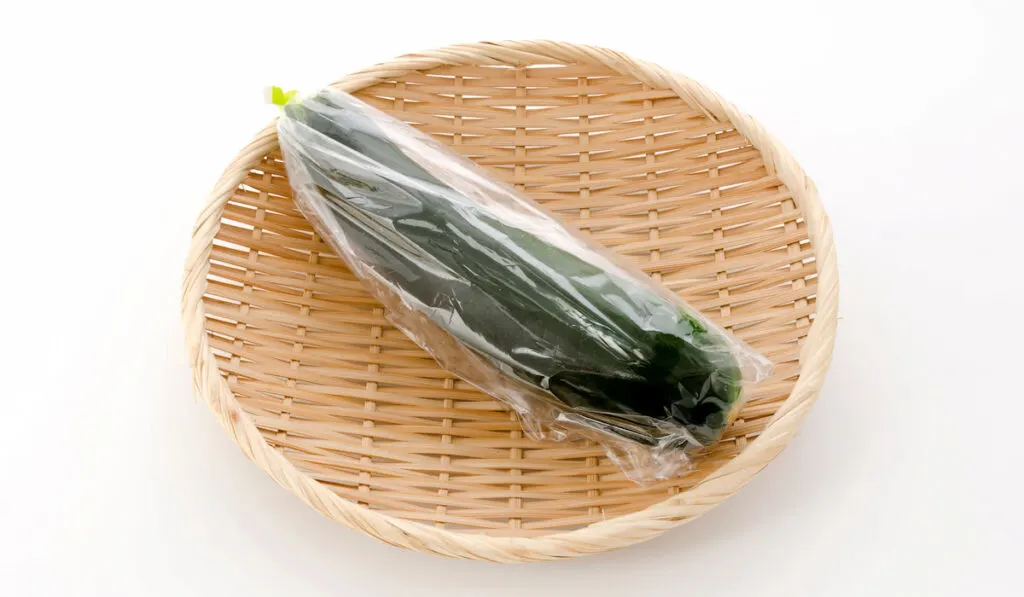 Fresh raw zucchini in plastic bag on a bamboo sieve on white background