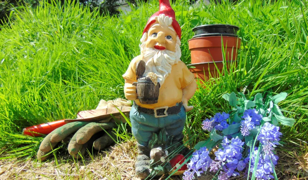 Garden gnome surrounded by grass and tools
