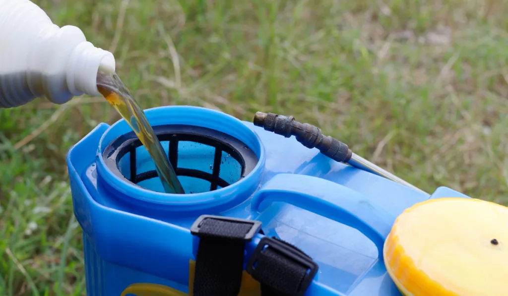 pouring herbicide water from bottle into tank sprayer
