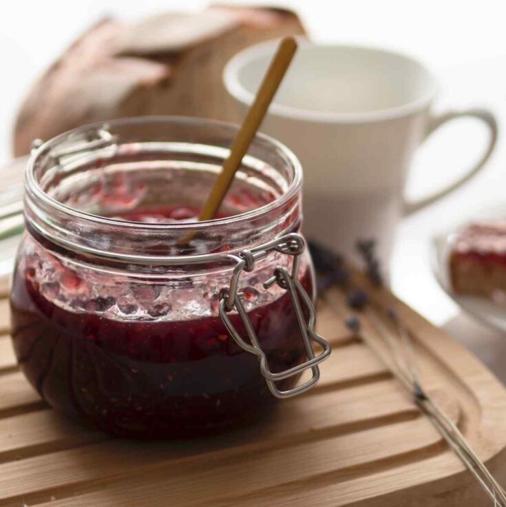 plum jam in a little jar with a wooden spoon, decorative items in the background