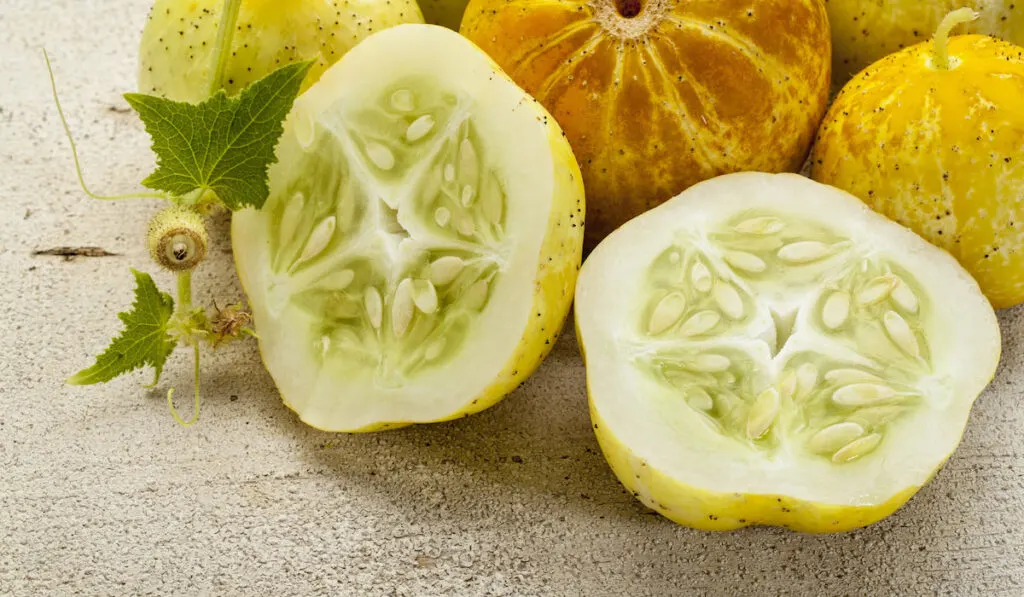 Sliced and whole lemon cucumbers on rough white wood surface