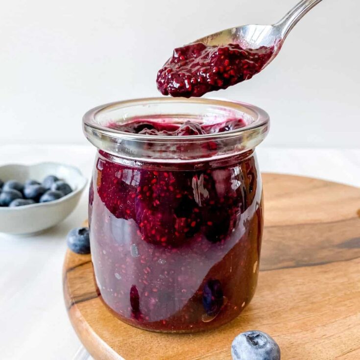 blueberry chia jam in a clear jar with a spoon lifting out a small portion