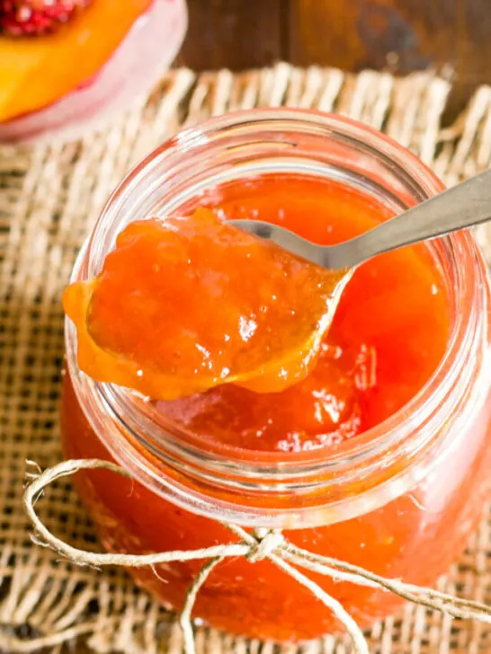 spoonful of peach jam being lifted out of a glass jar