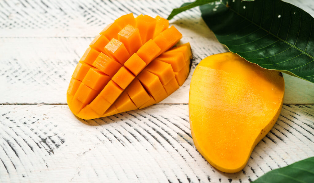 Fresh yellow mango fruit with leaves on white wood