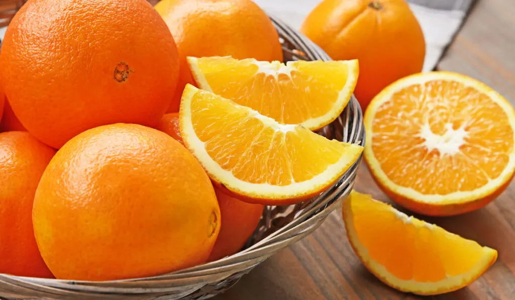 Whole and slices of Navel oranges in basket on wooden table