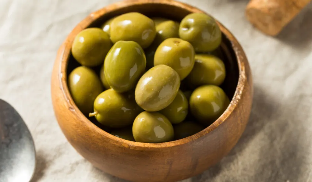 raw green organic olives in a wooden bowl