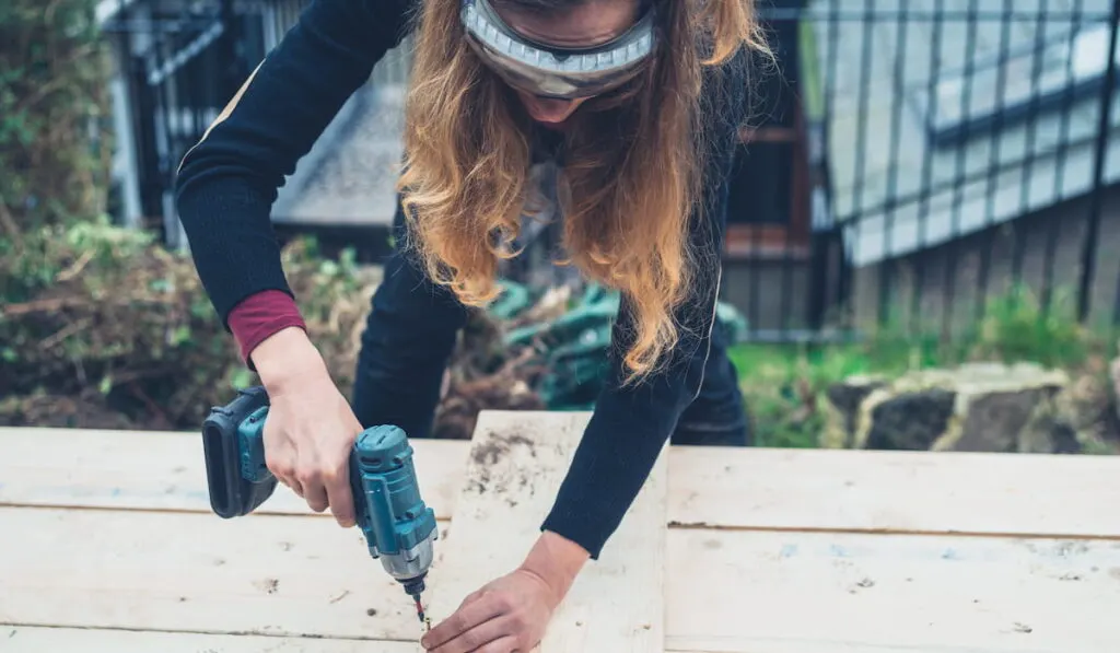A young woman is using an impact driver to make raised bed