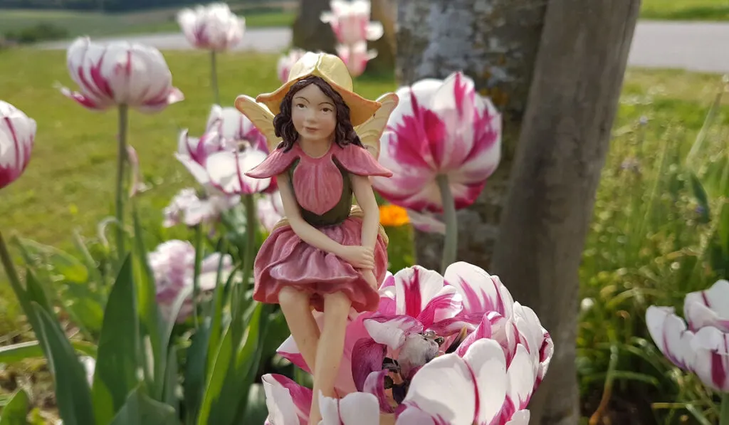 Miniature garden fairy statue in pink on tulip flowers on the background 