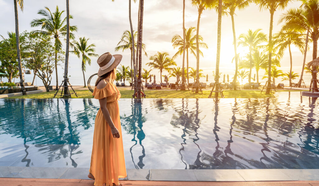 woman traveler relaxing and enjoying the sunset by a tropical resort pool 