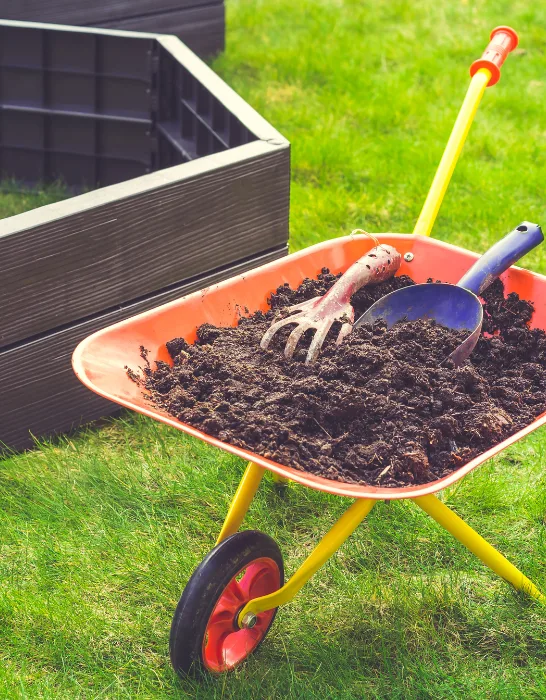 Garden-barrow-with-soil-and-empty-raised-beds-on-grass-prepared-for-filling-with-soil-ss230
