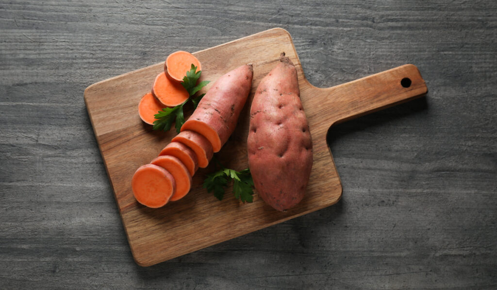 Sweet potatoes on wooden chopping board on gray background