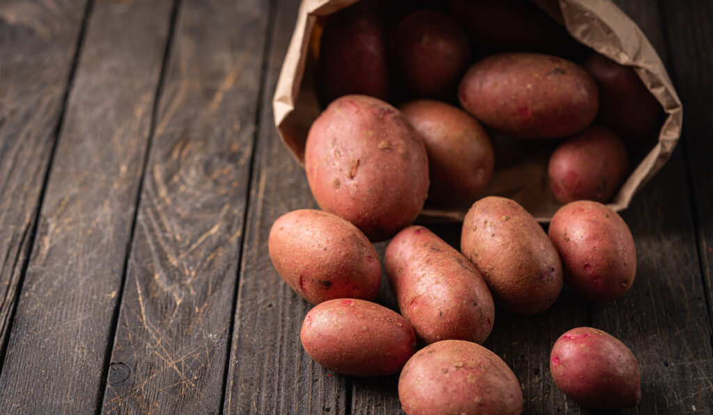 raw red potatoes in paper bags on wooden background