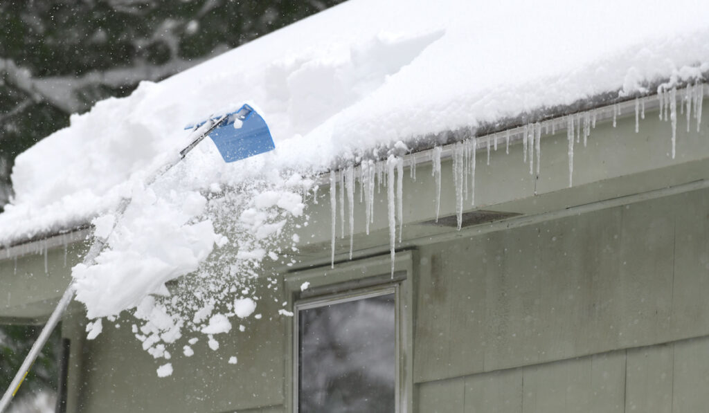 removing snow on the roof after snow storm using a rake
