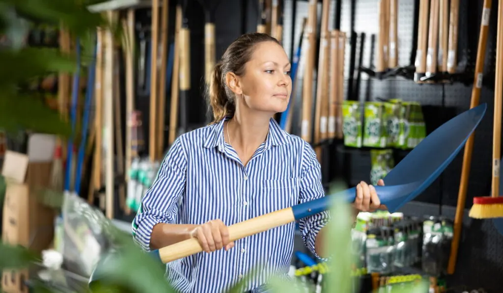 woman purchasing new spade or shovel  in gardening tools store 