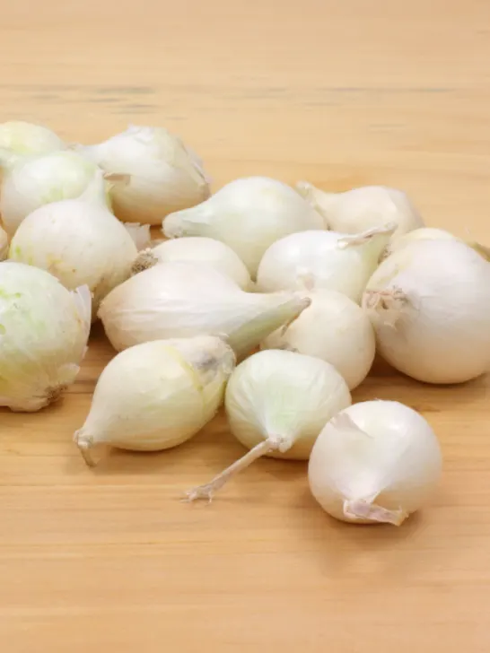 A small group of white boiling onions on a wood cutting board - ss230728