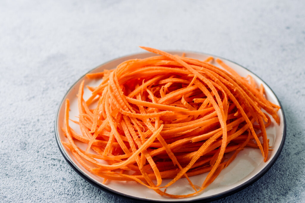 Raw carrot noodles on a plate on gray background