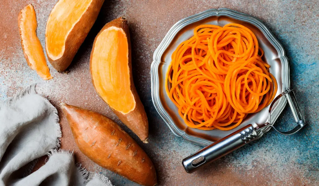 Spiralized sweet potato spaghetti, sweet potato and a peeler on rustic tone table 