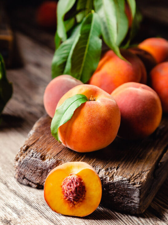 Peaches with leaves on dark wooden board with peach in halves with peach seed stone - ss231130
